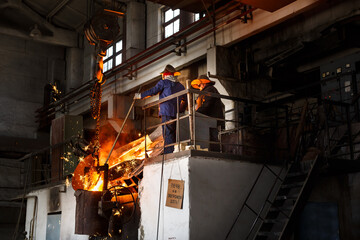 Industrial workers in protective gear operate furnace, handling molten metal at steel mill....