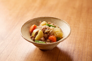 木のテーブルに肉じゃが、ベージュの皿