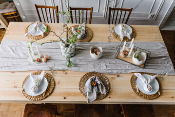 Setting table for Easter dinner with candles, ceramic plates with easter eggs in nest, Easter bunny made of linen napkin. Holidays celebration concept. From above place. Top view. Easter decor. Set up