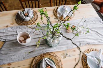 Setting table for Easter dinner with candles, ceramic plates with easter eggs in nest, Easter bunny...