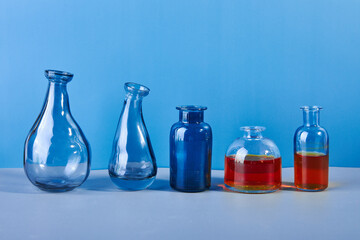 Set of various muted colored glass and metal bottles and vases on a blue background.