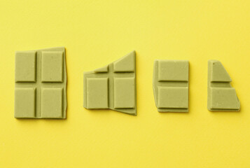 Pieces of tasty matcha chocolate bars on yellow background, flat lay