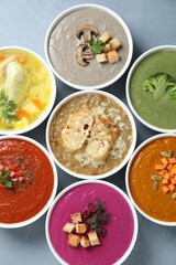 Tasty broth and different cream soups in bowls on table, flat lay