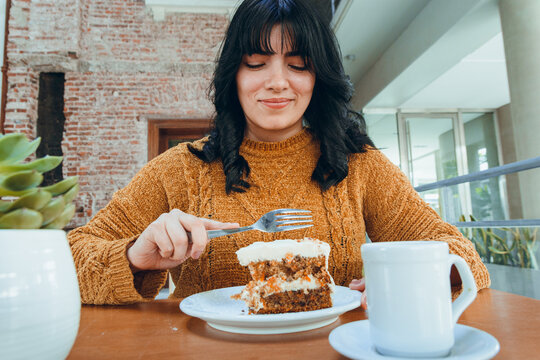 portrait of young very happy latin woman sitting eating carrot cake in u restaurant