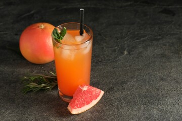 Tasty grapefruit drink with ice and mint in glass on dark textured table. Space for text