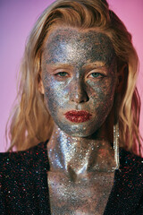 portrait of beautiful blonde woman with glitter makeup and sparkling dress posing on pink gradient