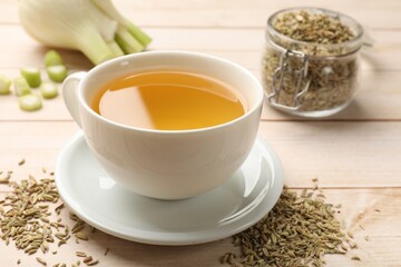Fennel tea in cup, seeds and fresh vegetable on light wooden table, closeup