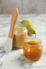 Tasty baby food in jars, pear and spoon on white marble table