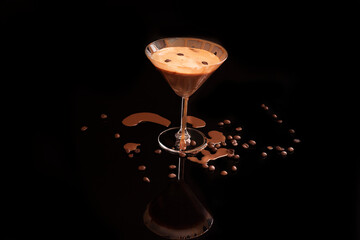 Spilled on the table and running down the glass Espresso Martini cocktail in a martini glass decorated with coffee beans on a black background in a low key.

