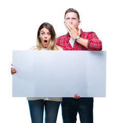 Young couple together holding blank banner over isolated background cover mouth with hand shocked with shame for mistake, expression of fear, scared in silence, secret concept