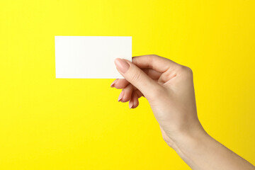 Obraz premium Woman holding blank business card on yellow background, closeup. Mockup for design