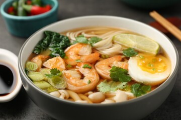 Delicious ramen with shrimps and egg in bowl on grey table, closeup. Noodle soup
