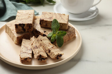 Pieces of tasty chocolate halva and mint on white marble table, closeup. Space for text