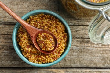 Whole grain mustard in bowl and spoon on wooden table, top view