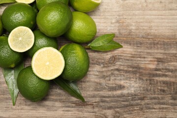 Pile of fresh limes and green leaves on wooden table, flat lay. Space for text