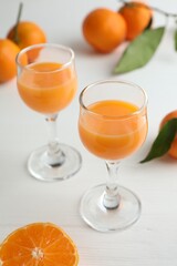 Tasty tangerine liqueur in glasses and fresh citrus fruits on white table