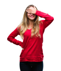 Obraz na płótnie Canvas Young beautiful blonde woman wearing red sweater over isolated background smiling and laughing with hand on face covering eyes for surprise. Blind concept.