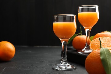 Tasty tangerine liqueur in glasses and fresh citrus fruits on black textured table. Space for text