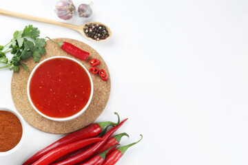 Spicy chili sauce in bowl and ingredients on white background, flat lay. Space for text