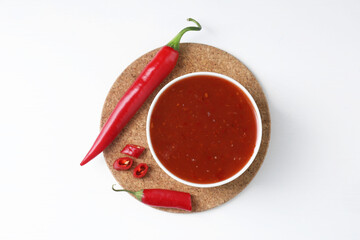 Spicy chili sauce in bowl and fresh peppers on white background, top view