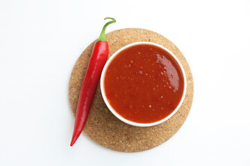 Spicy chili sauce in bowl and fresh pepper on white background, top view