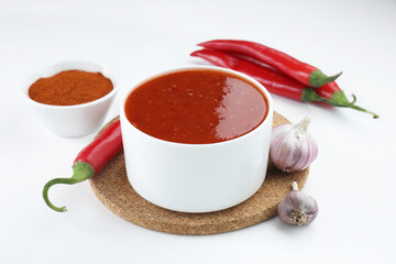 Spicy chili sauce in bowl and ingredients on white background