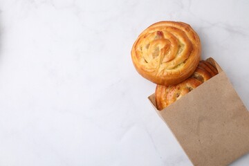 Paper bag with delicious rolls on white marble table, top view and space for text. Sweet buns