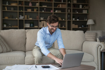 Happy millennial business man, individual entrepreneur does his own bookkeeping, sit at table...