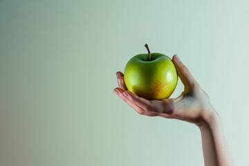 Elegant hand presenting a ripe green apple on a neutral background, highlighting the simplicity and purity of organic produce
