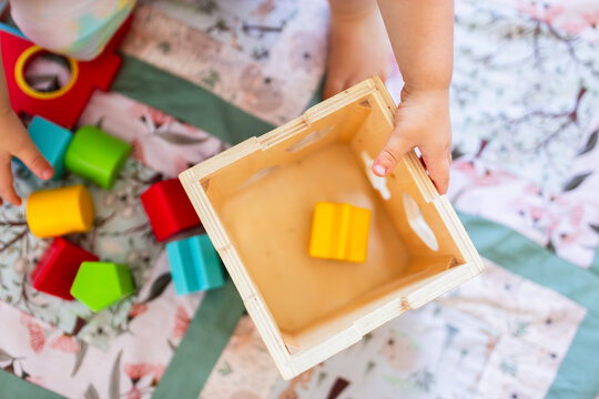 Toddler playing with coloured shapes in wooden shape sorter box
