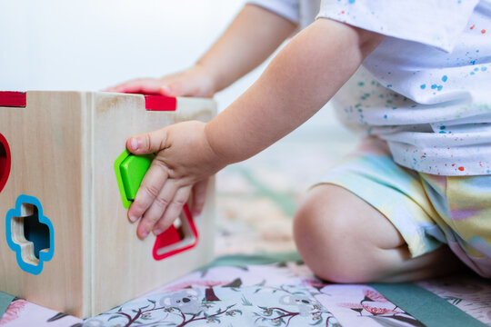 Toddler posting coloured shapes into wooden shape sorter box