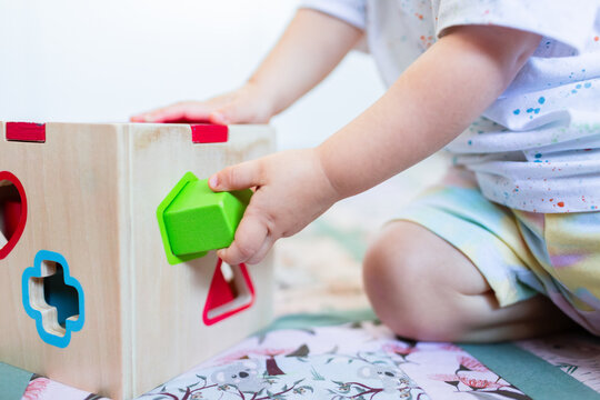 Toddler posting coloured shapes into wooden shape sorter box