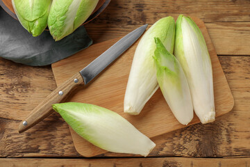 Fresh raw Belgian endives (chicory), board and knife on wooden table, top view - obrazy, fototapety, plakaty