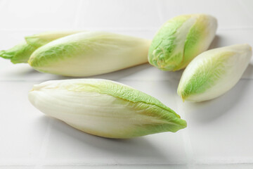 Fresh raw Belgian endives (chicory) on white tiled table, closeup