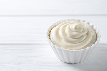 Fresh mayonnaise sauce in bowl on white wooden table, closeup. Space for text