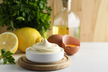 Fresh mayonnaise sauce in bowl and ingredients on white wooden table, space for text