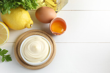 Fresh mayonnaise sauce in bowl and ingredients on white wooden table, flat lay. Space for text