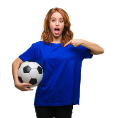 Young beautiful woman over isolated background holding soccer football ball with surprise face pointing finger to himself