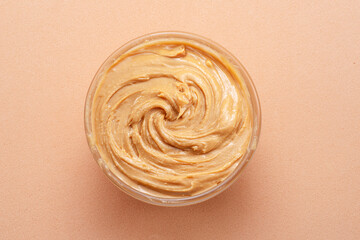 Bowl of peanut butter on beige background. Top view.