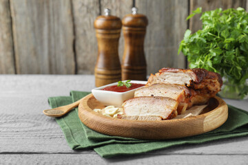 Pieces of baked pork belly served with sauce on grey wooden table, space for text