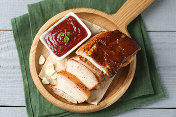 Pieces of baked pork belly served with sauce on grey wooden table, top view