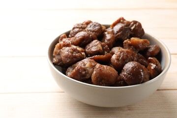 Roasted edible sweet chestnuts in bowl on light wooden table, closeup
