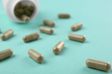 Bottle and vitamin capsules on turquoise background, closeup