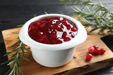 Cranberry sauce in bowl, fresh berries and rosemary on table, closeup