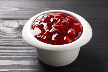 Fresh cranberry sauce in bowl on black wooden table, closeup