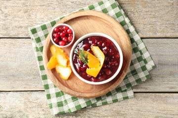 Cranberry sauce in bowl, fresh berries, rosemary and orange peels on wooden table, top view