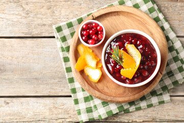Cranberry sauce in bowl, fresh berries, rosemary and orange peels on wooden table, top view. Space for text