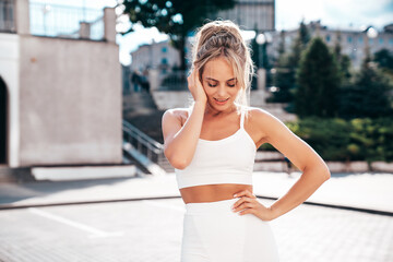 Fototapeta premium Young beautiful smiling female in trendy summer white cycling shorts and tank top clothes. Sexy carefree woman posing in street. Positive model. Cheerful and happy. Slim and fit body