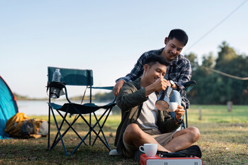 Gay LGBTQIA couple sitting on picnic chair drinking tea and coffee while camping on vacation holiday