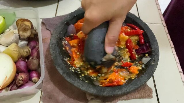a woman traditionally grinds chilies in a stone mortar to make chili sauce